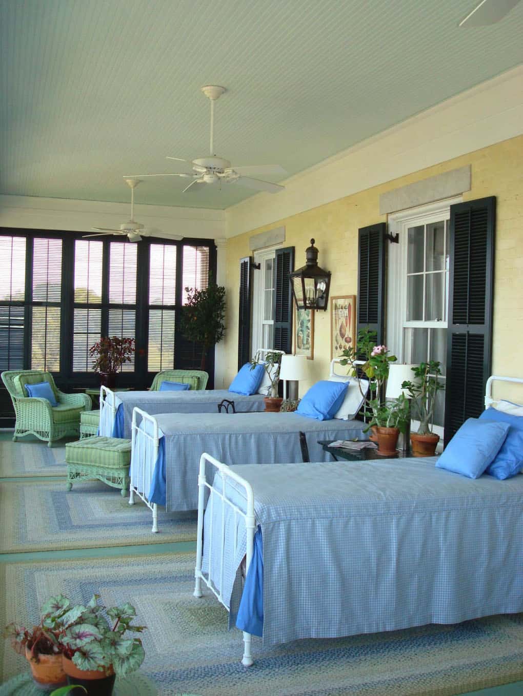 large sleeping porch with three beds with clue sheets and pillows, yellow hours with black shutters