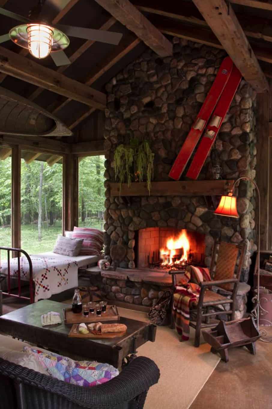 sleeping porch with large windows and fireplace with skis, a chair with a blanket and bed in the corner with a white and red blanket. 