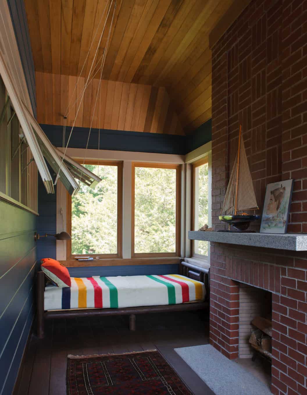 small sleeping porch with daybed with colorful striped blanket and a fireplace with a boat on the mantle 