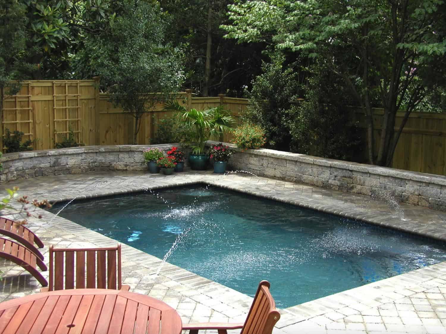 small rectangle pool with water spouts, and trees, a privacy fence and a sitting area 
