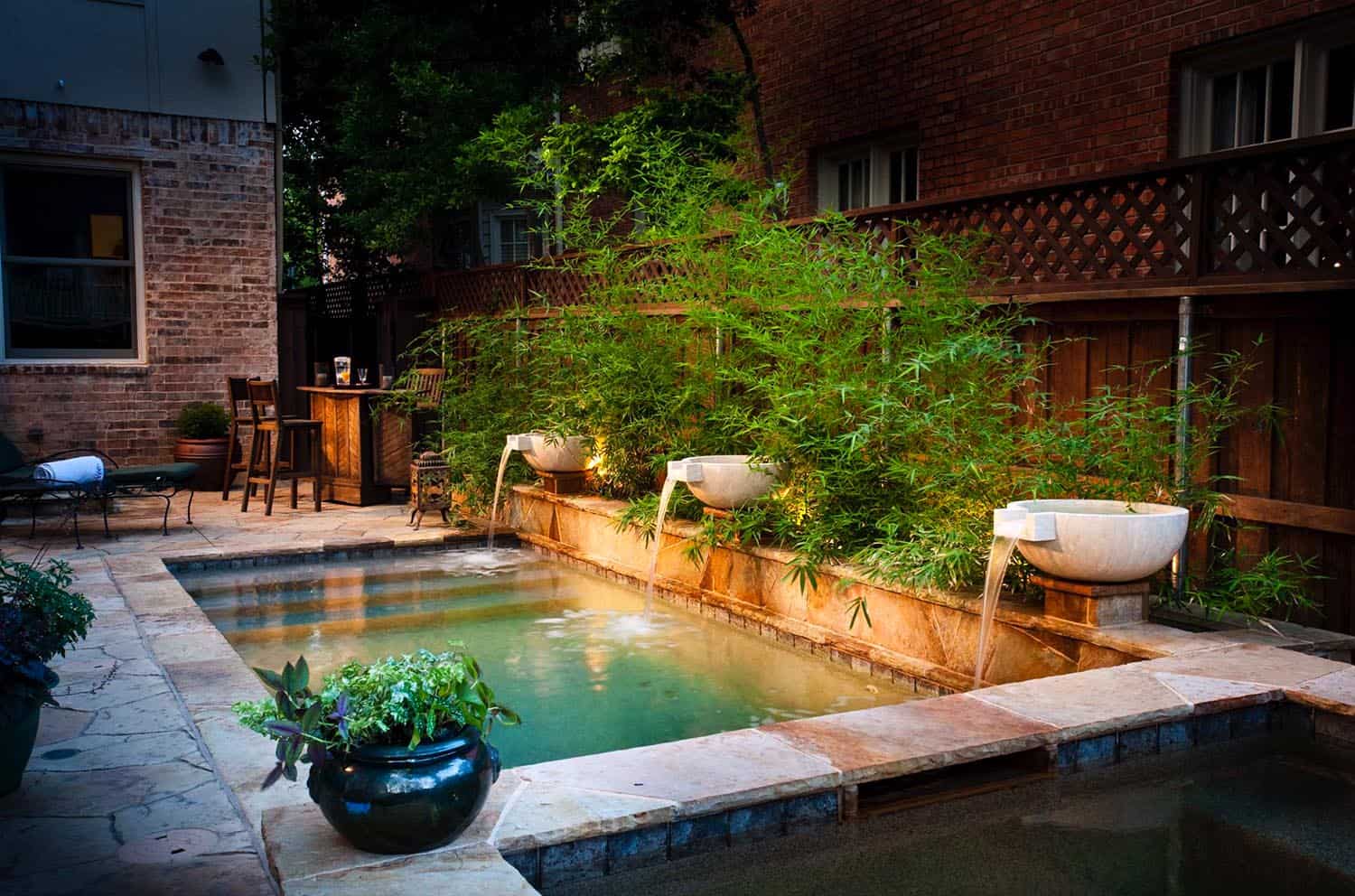 rectangle small pool with three water spouts pouring in with trees and bushes in background 