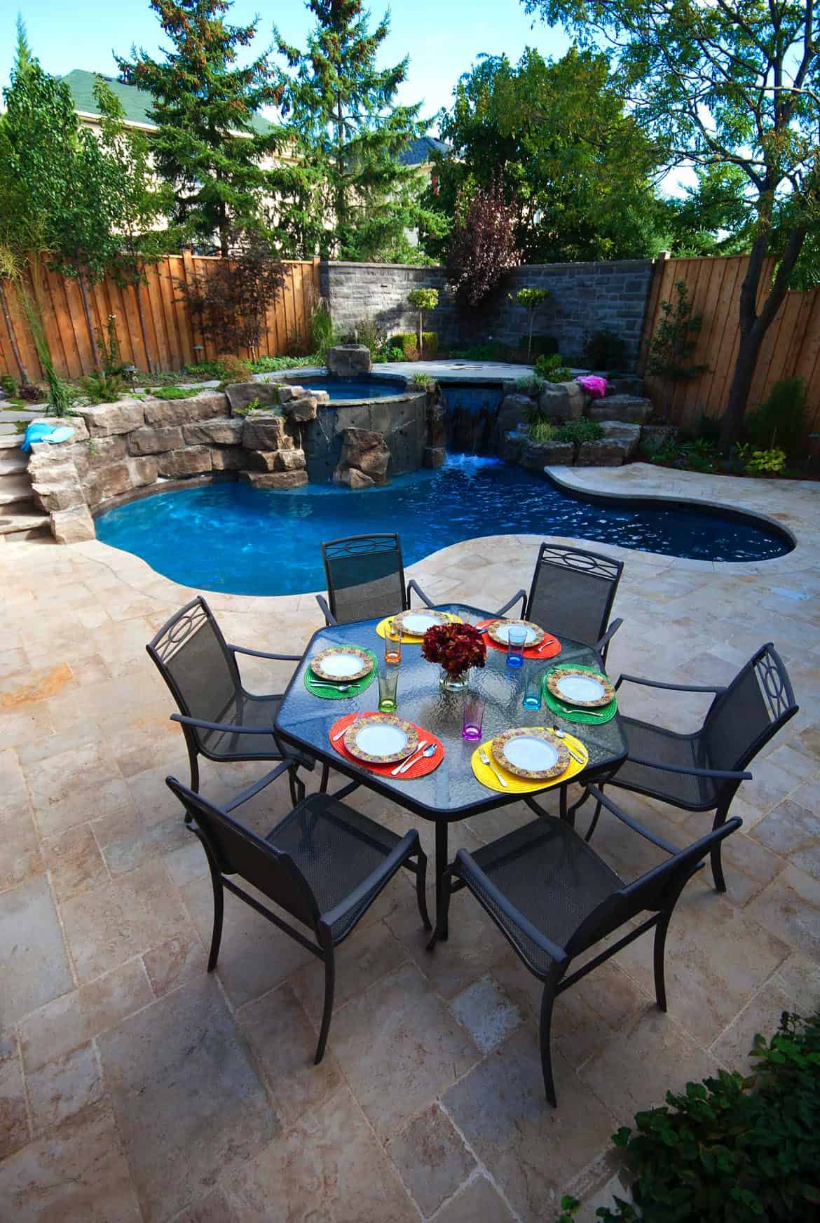 small custom shaped pool with rock formation waterfall and a sitting area with colorful plates 