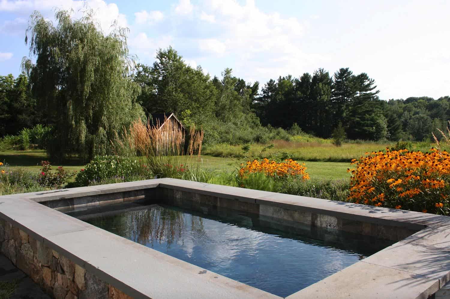 pool with rock siding overlooking grassy area with barn and flowers