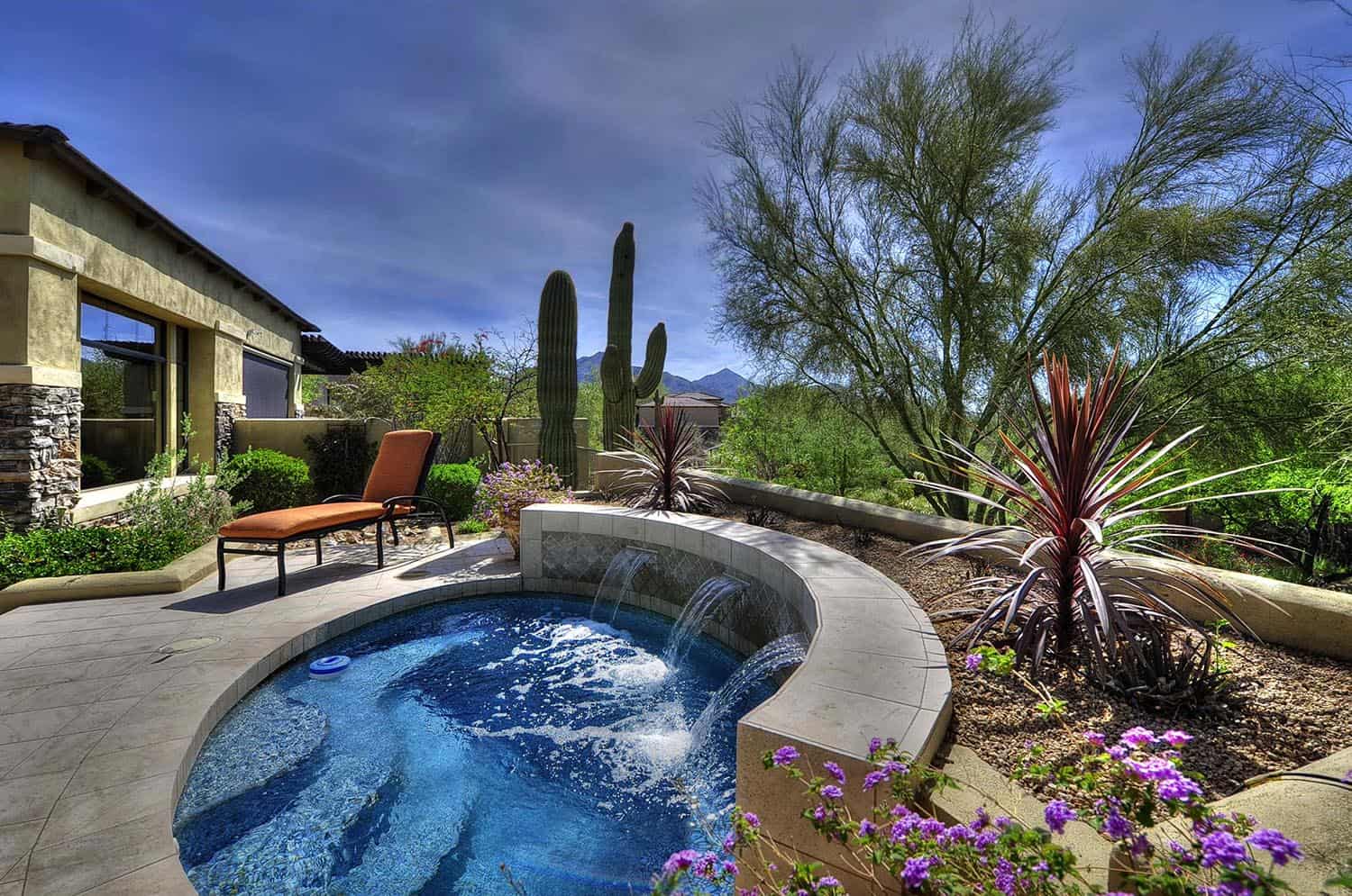 small pool with water spout pouring out of wall, desert background with house and sitting area 