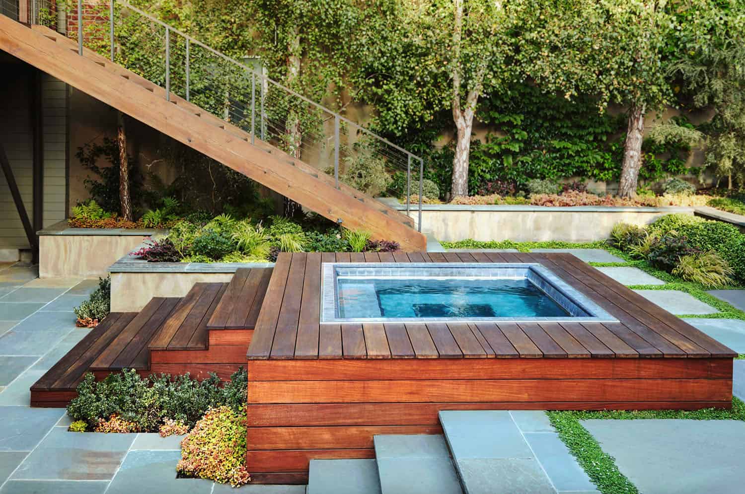 stairs coming down from a deck that lead to an above ground hot tub with a custom deck around it. trees in background. 