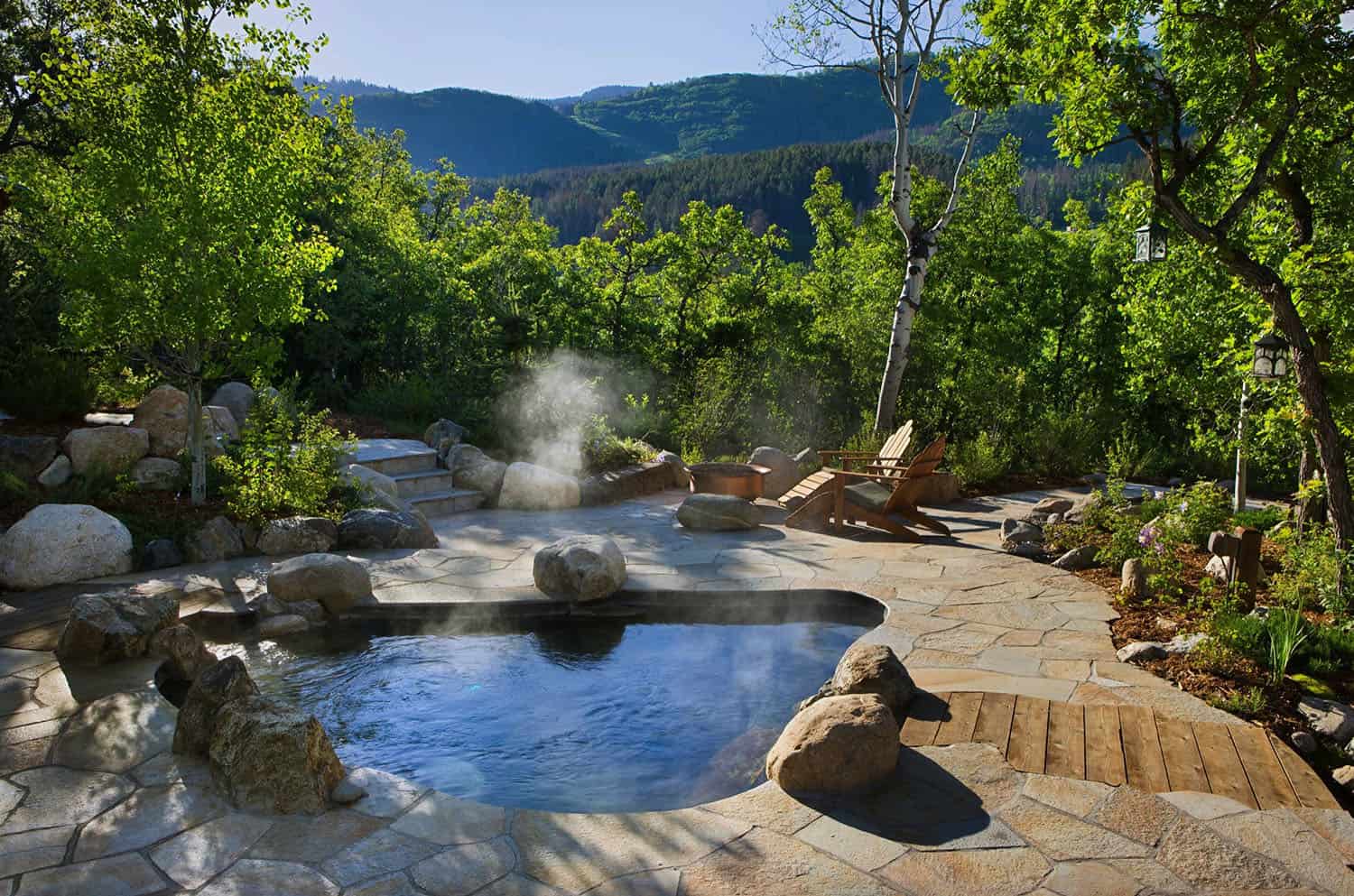 outdoor hot tub with rock design and boulders around the edge of the hot tub with mountains and trees in the background 