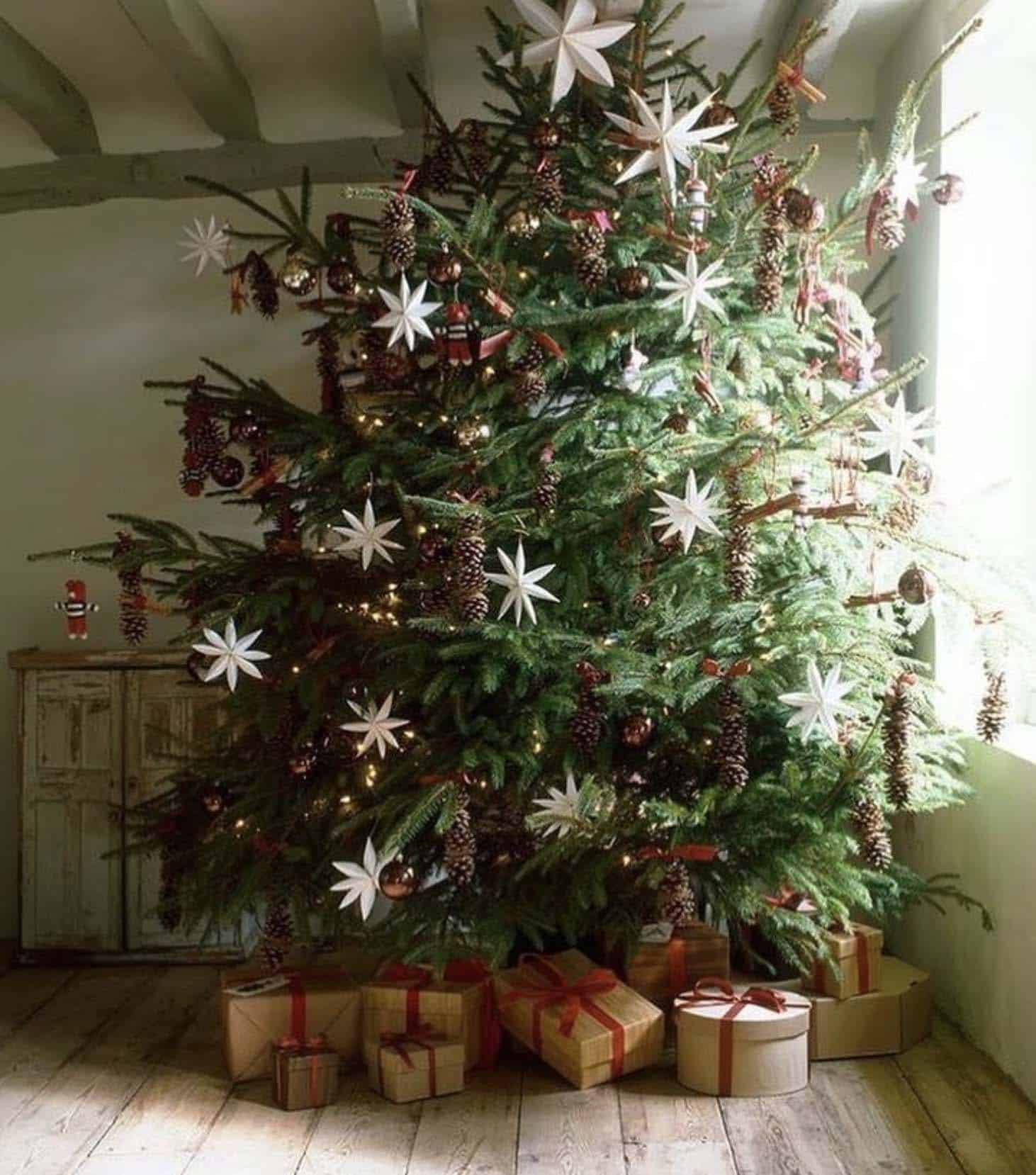 beautiful christmas tree with white paper stars and pinecones and presents underneath