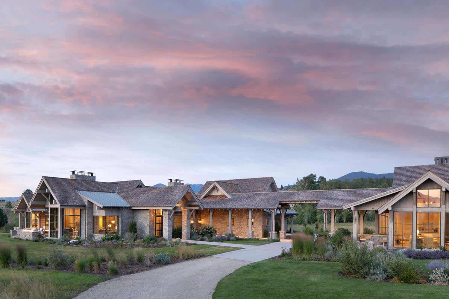 rustic mountain home exterior with a long driveway at dusk