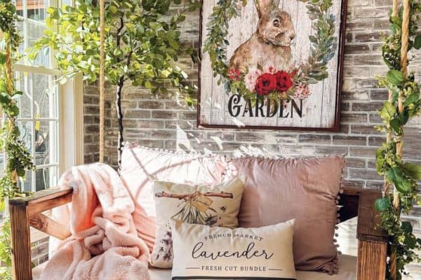 front porch with a porch swing, pillows and a spring sign on the wall