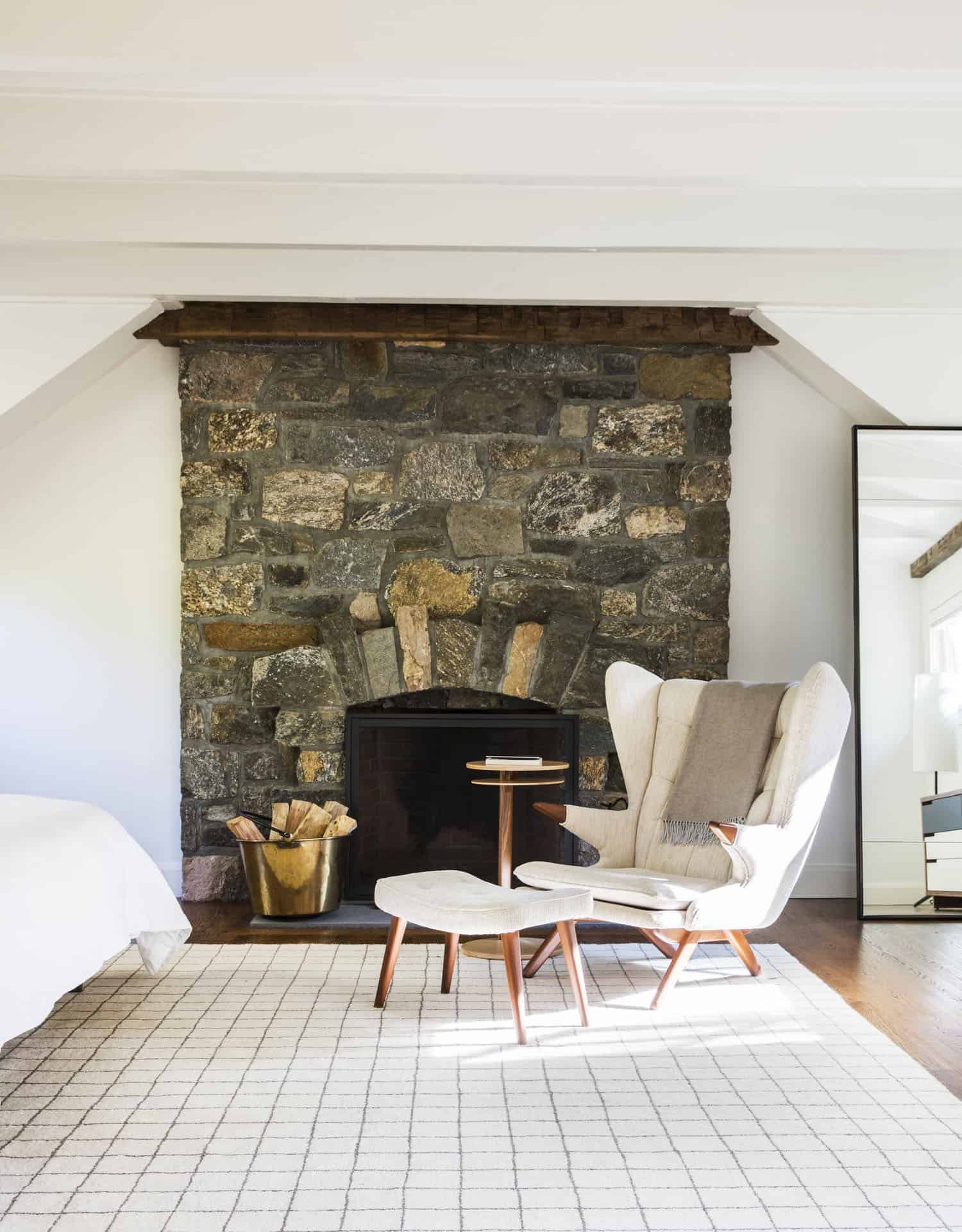 farmhouse bedroom with a stone fireplace and lounge chair with an ottoman