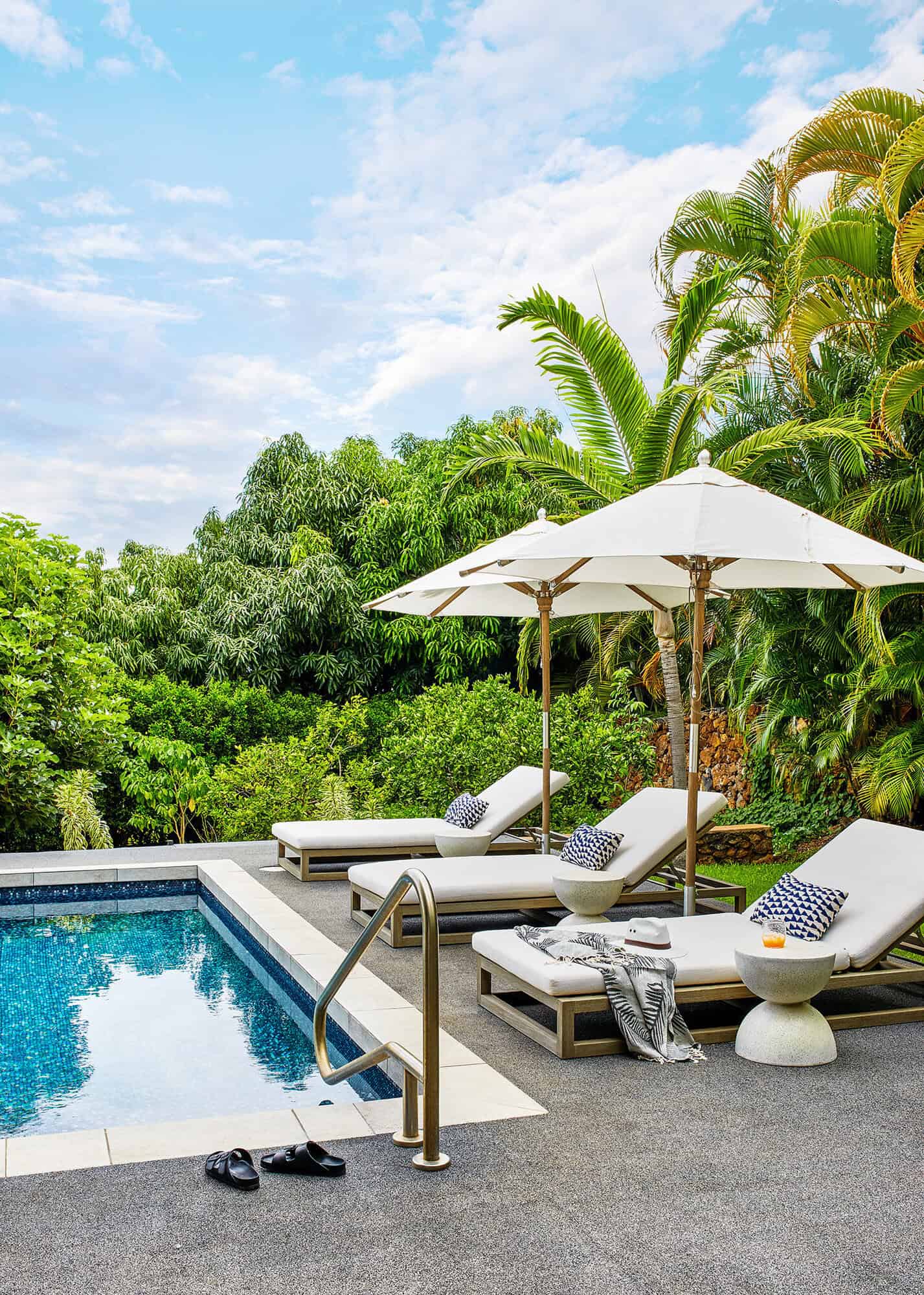 outdoor pool with sun loungers and white umbrellas surrounded by tropical gardens