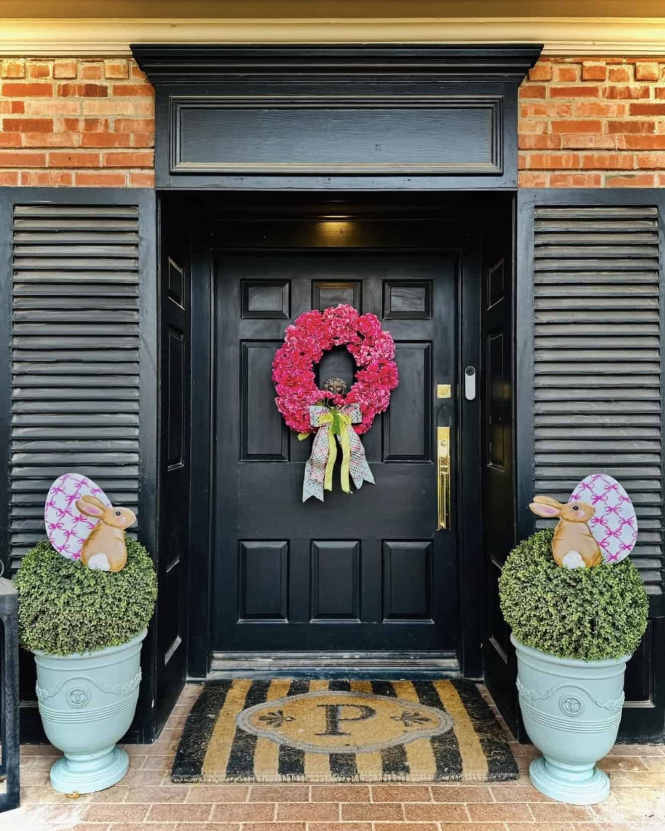 front porch with a pink wreath and large wooden bunnies with easter eggs in urns