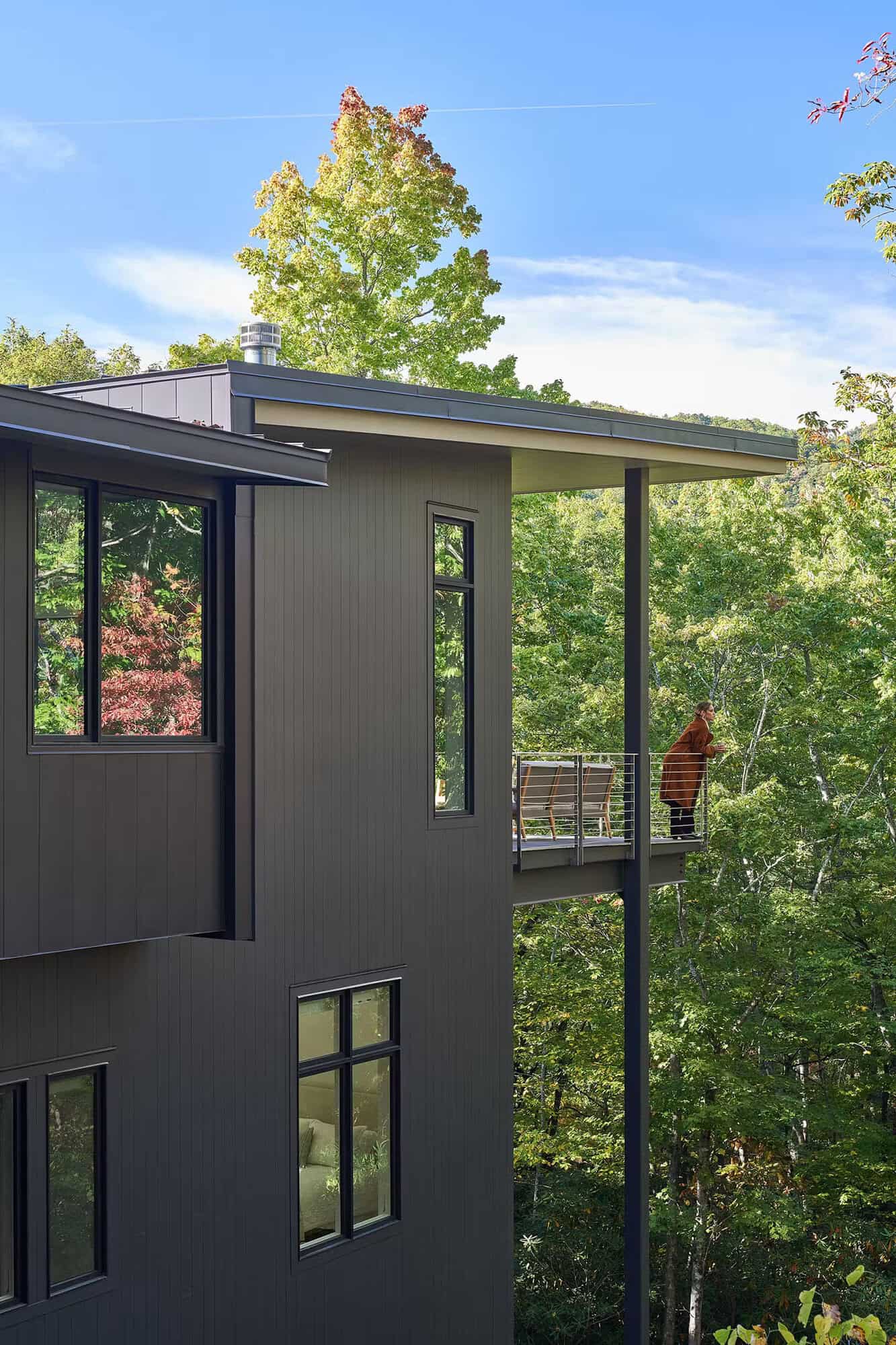 modern treehouse-like home exterior with a balcony overlooking the forest