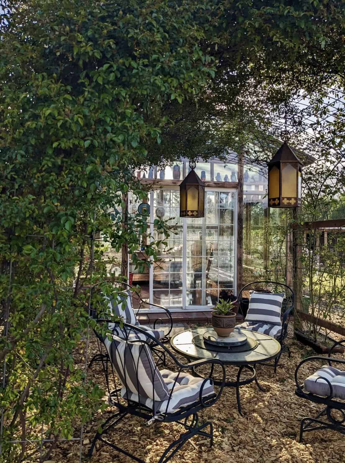 garden patio with lights hanging from the trees and a greenhouse in the backdrop
