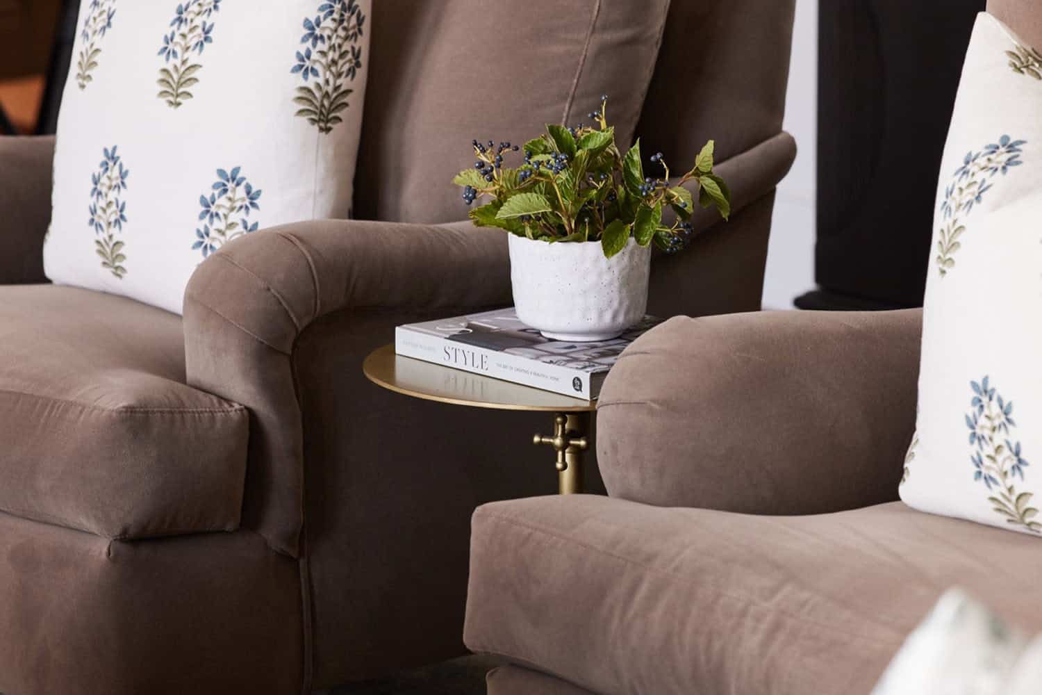 A pair of brown chairs with pillows and a plant on the table.