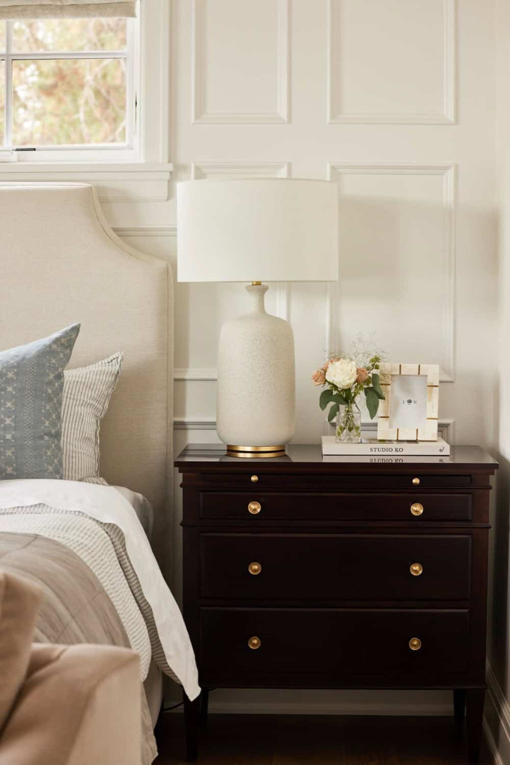 A bedroom with a white bed, nightstand and lamp.