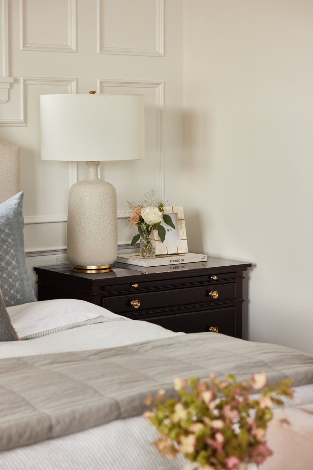 A bedroom with a white bed, nightstand and lamp.