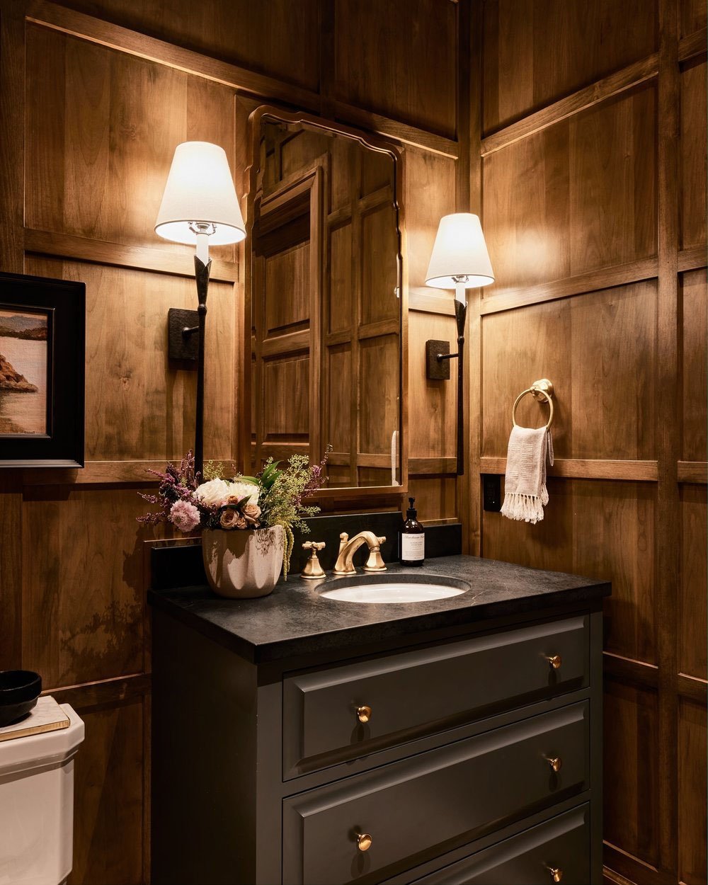 A powder room with wood paneling and a black counter top.