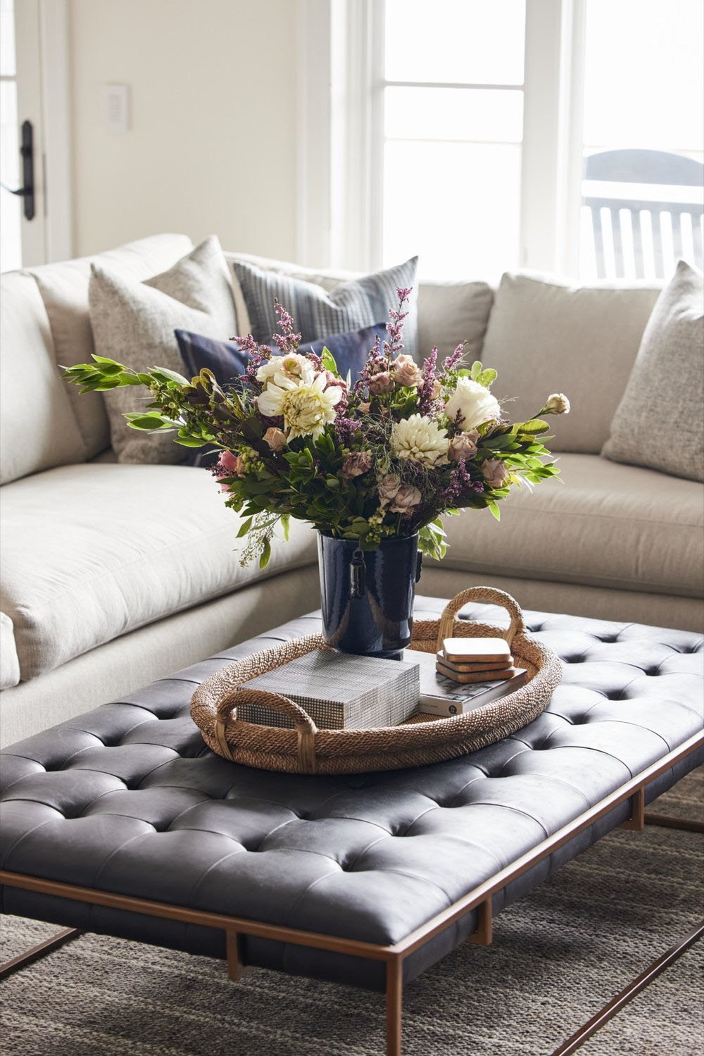 A family room with a sofa, coffee table, and vase of flowers.