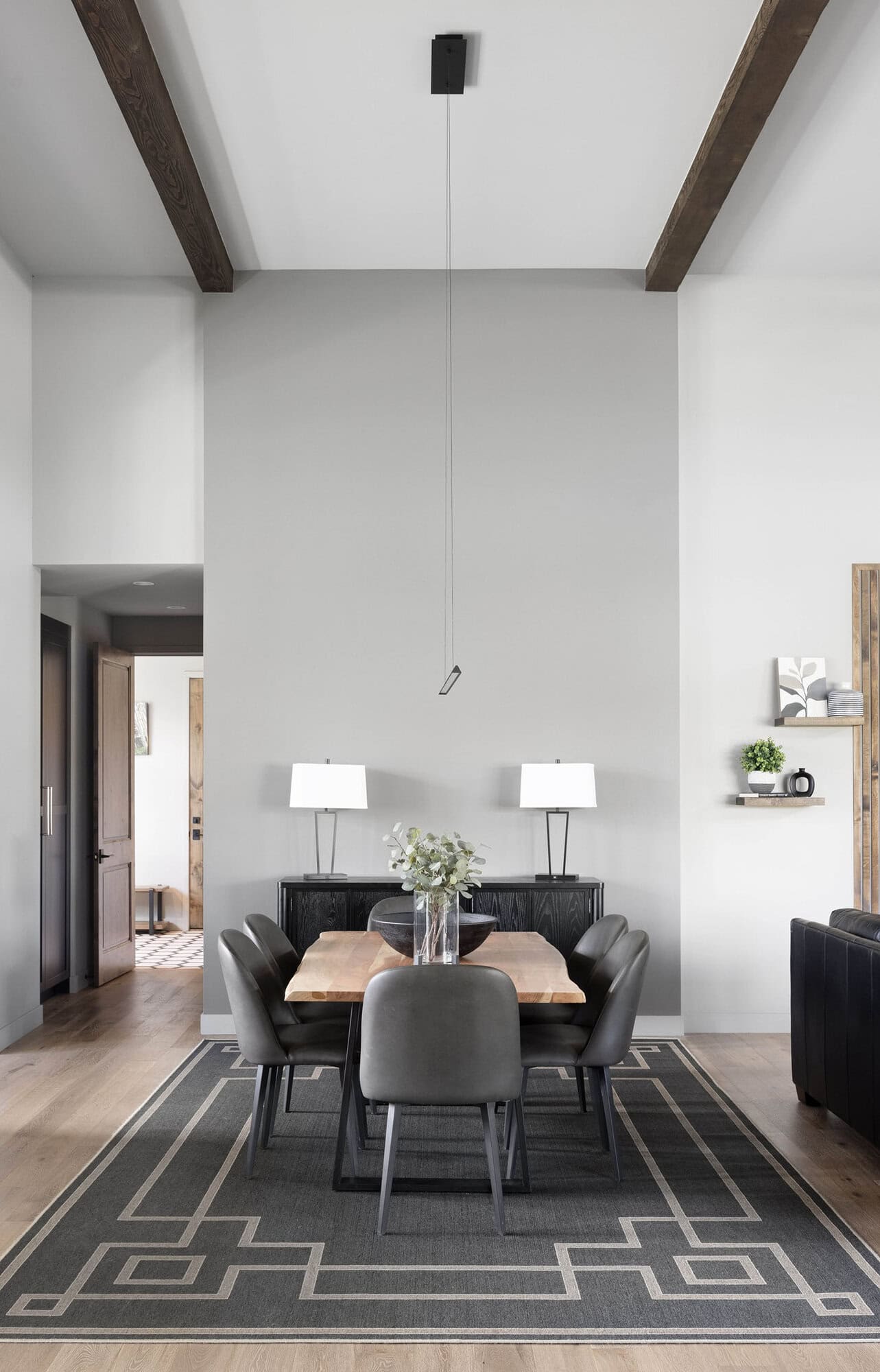 A modern dining room with a wooden ceiling and a black rug.