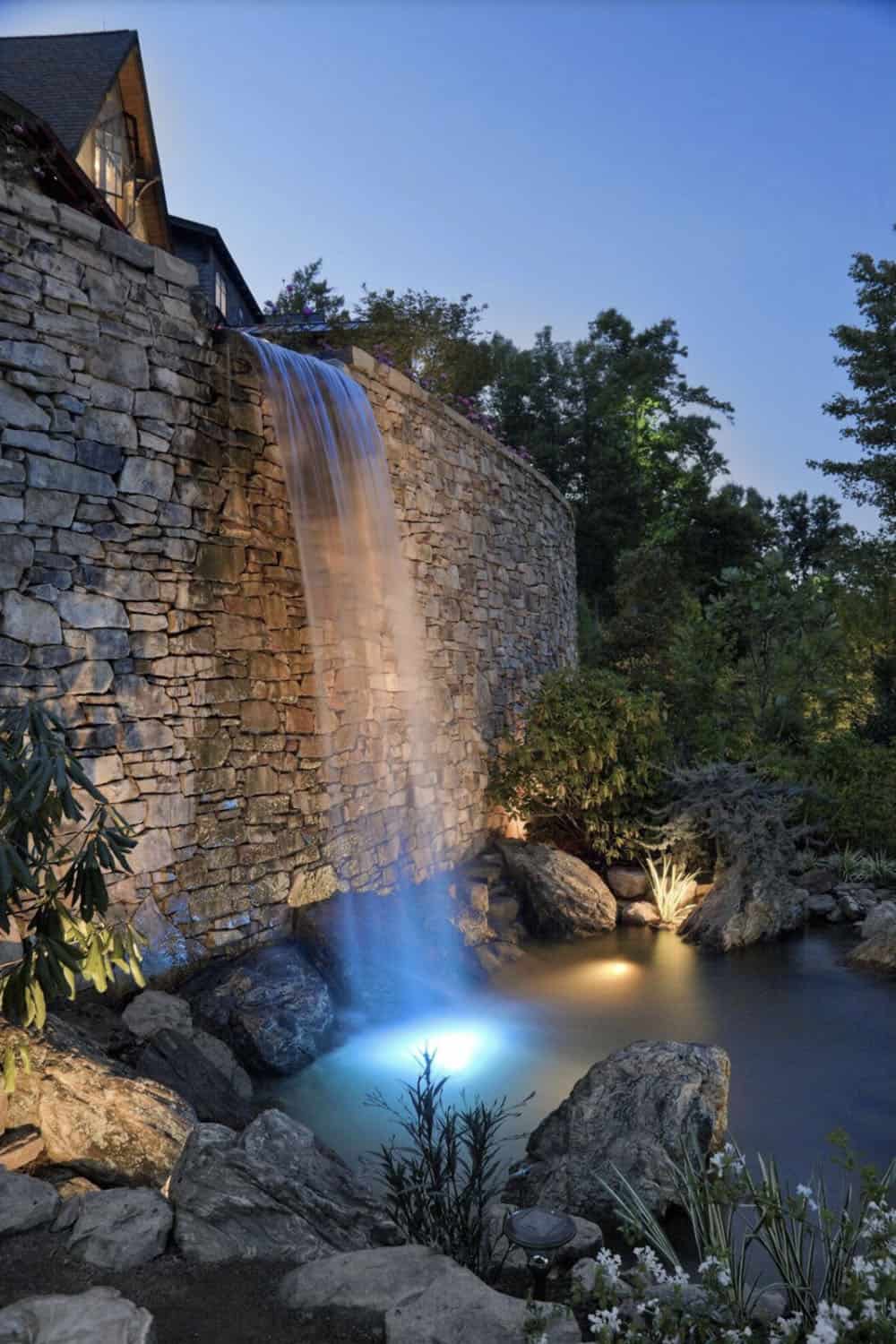 modern rustic mountain home exterior with a waterfall at dusk