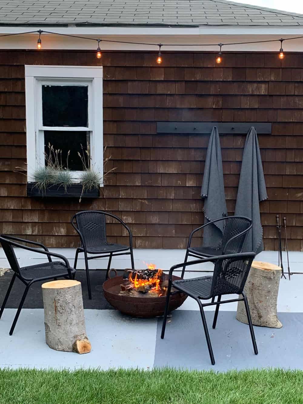 small backyard patio with modern chairs, wood stump side tables, and a fire pit