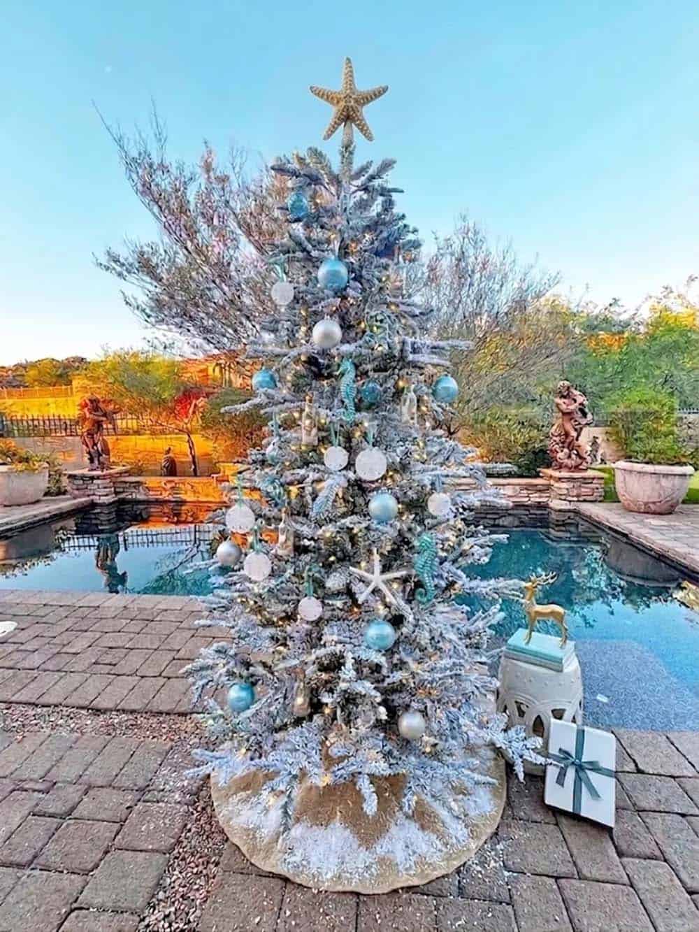 Flocked Christmas tree with starfish topper and blue coastal ornaments beside a pool