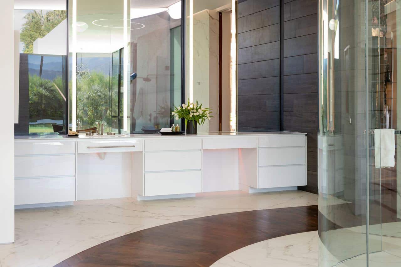 A bathroom with a large glass shower and a circular mirror.