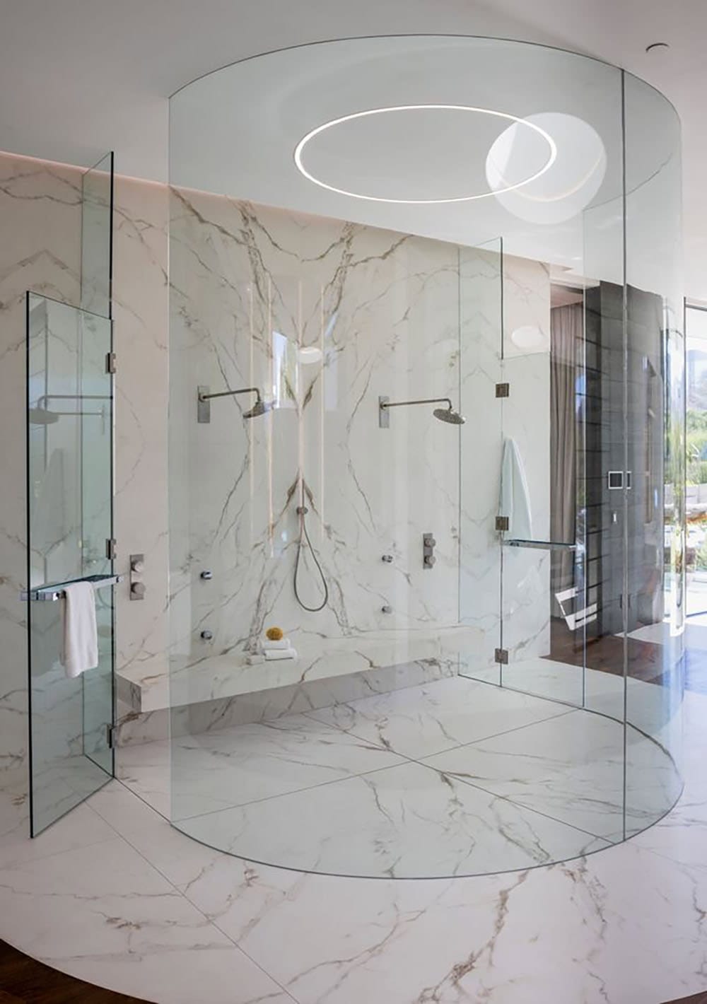 A bathroom with a large glass shower and a circular mirror.