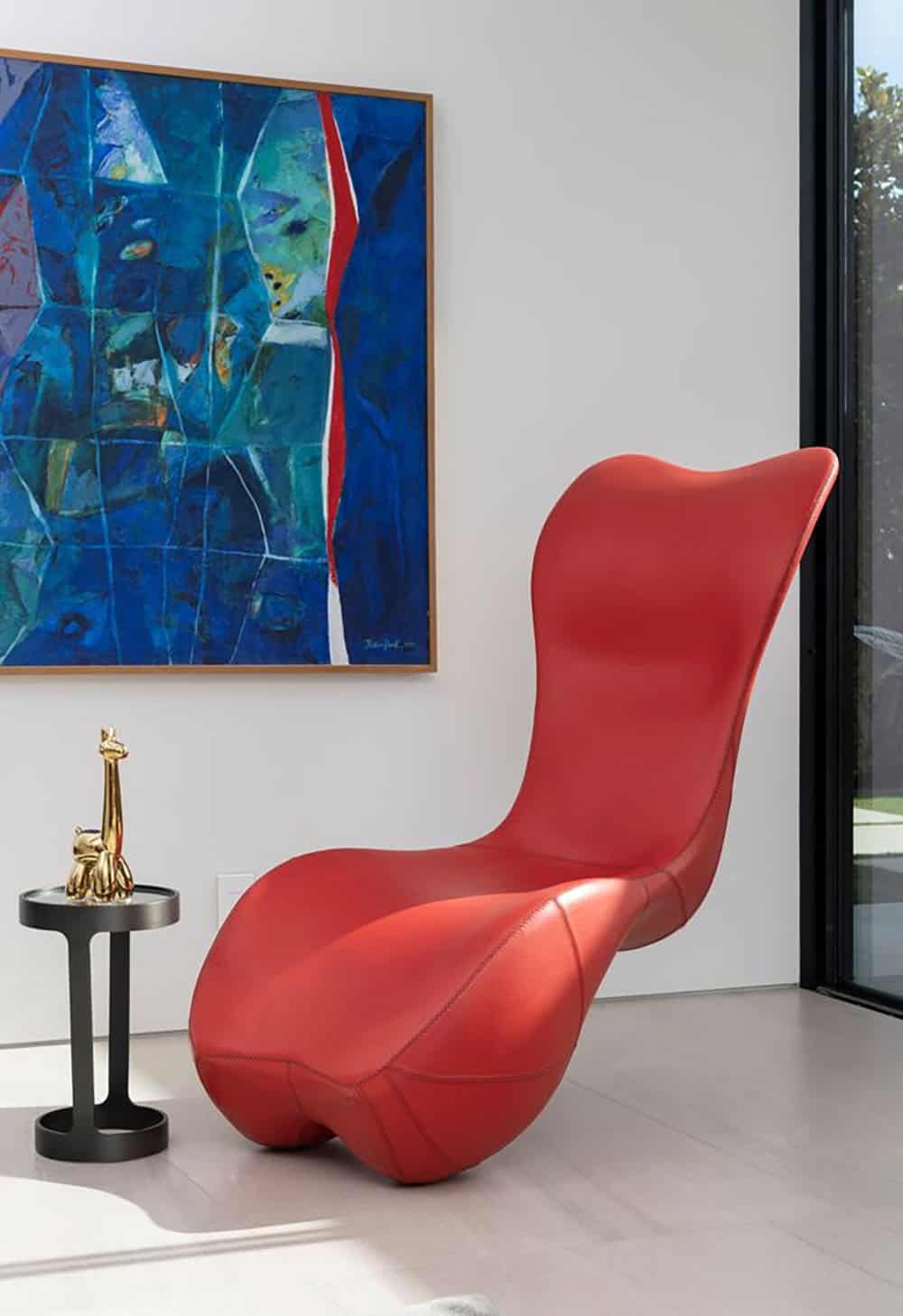 A red chaise lounge in a home office with a painting.