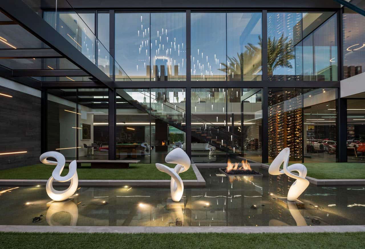 The modern home has a glass wall and a fountain.