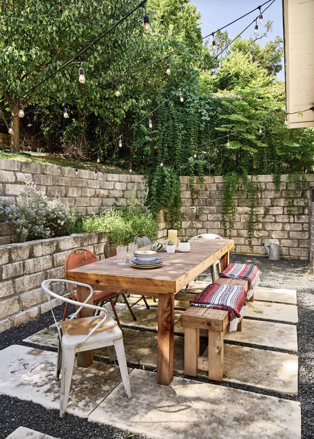 backyard patio with a stone terrace wall and outdoor dining with string lights
