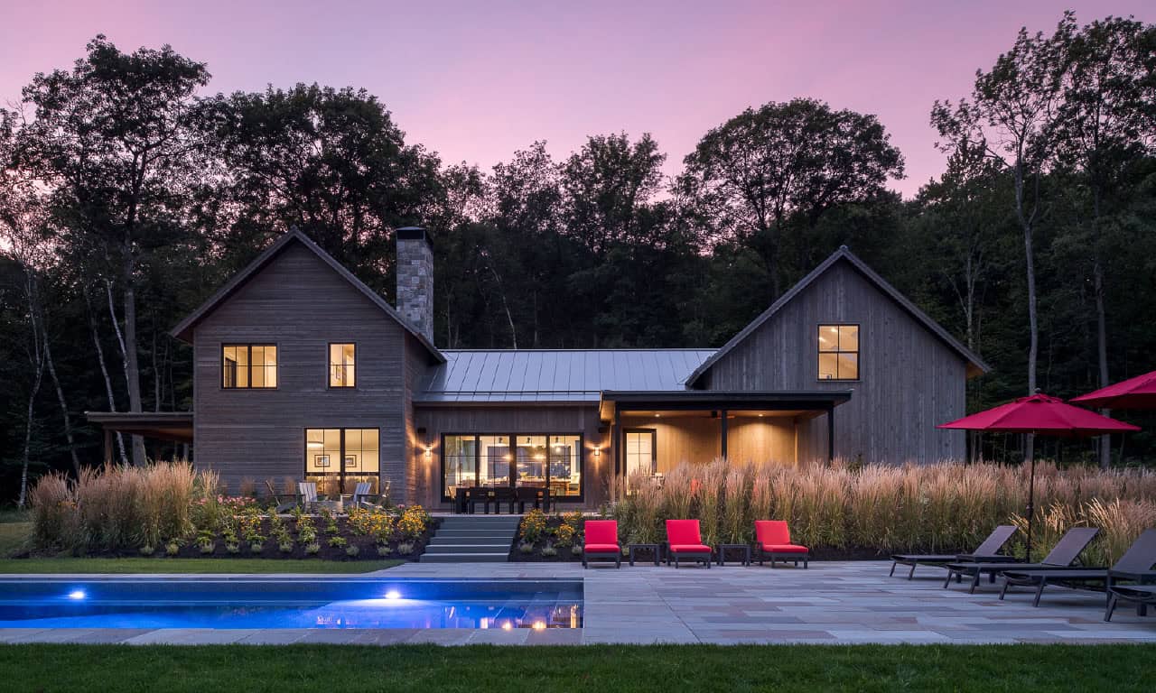 modern rustic home exterior with a pool at dusk