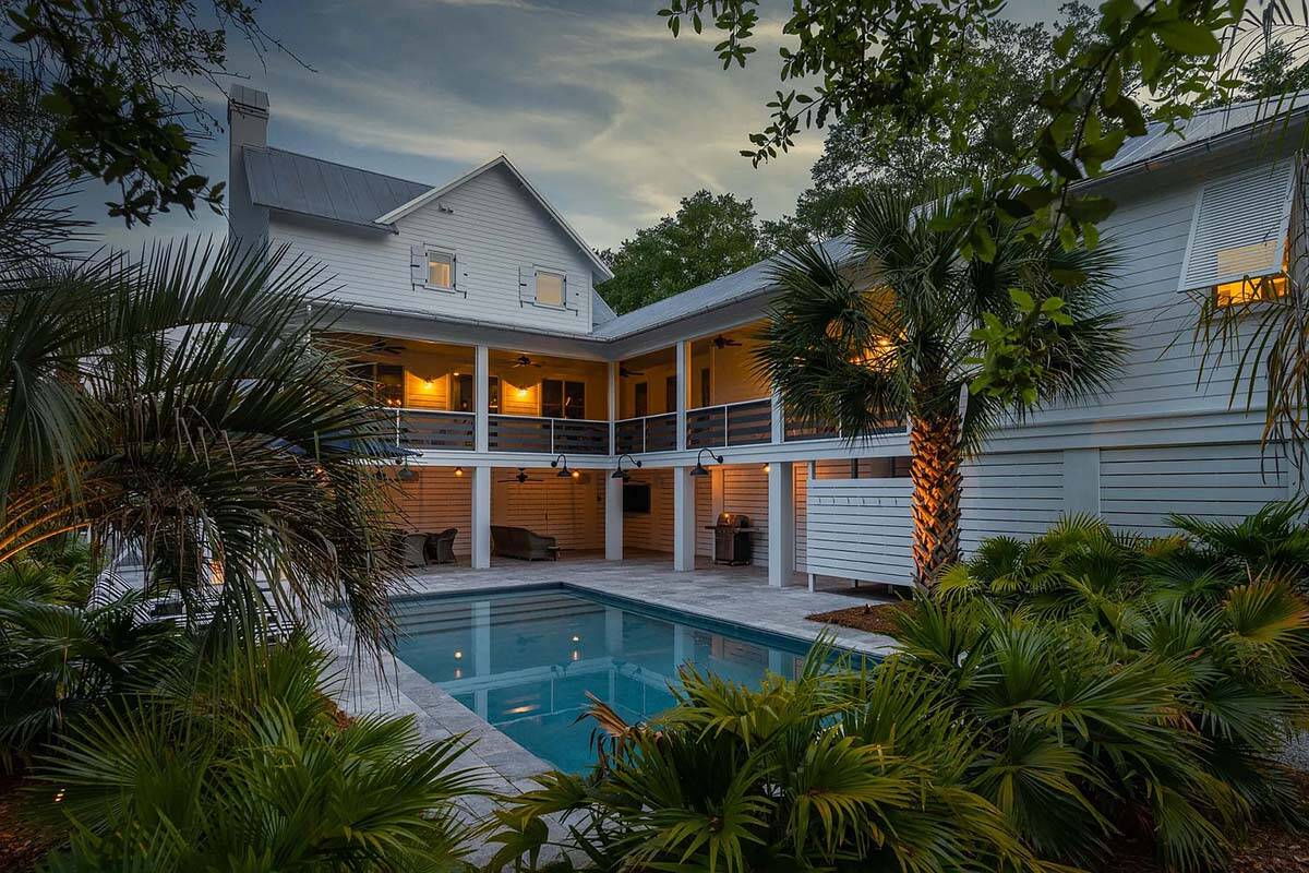 coastal style house exterior with a pool at dusk