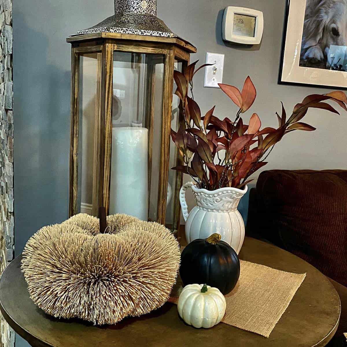 Fall table decor with a lantern, pumpkins, and a vase of artifical leaves