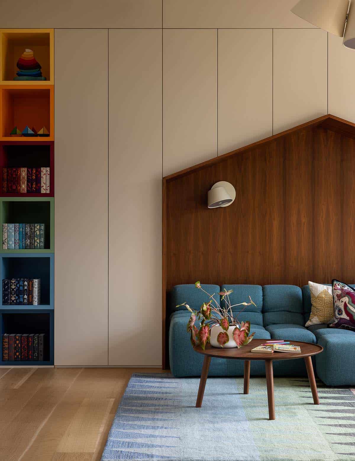 modern kids' lounge with a blue sectional a walnut house-shaped nook, and colorful cubby bookshelves