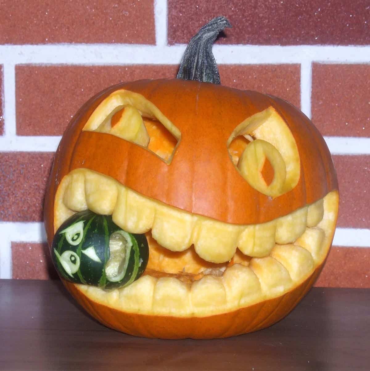 large pumpkin carving with a small green pumpkin in its mouth
