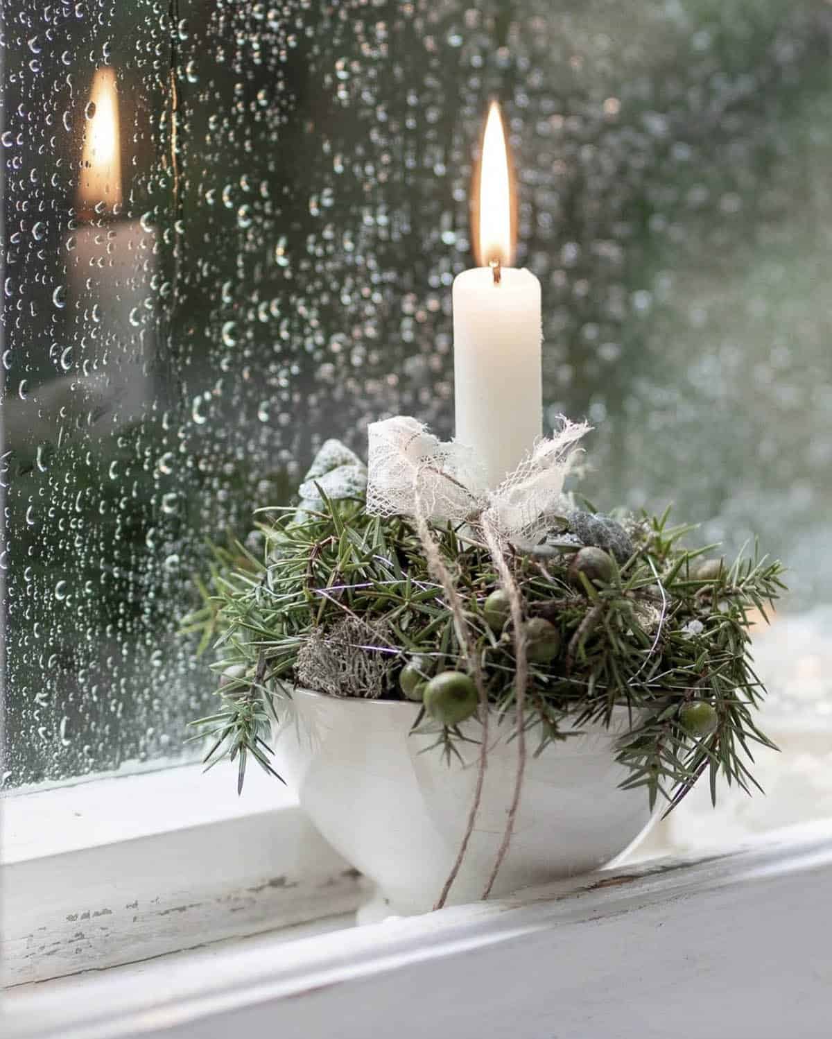 christmas candle in a bowl of greenery in the window