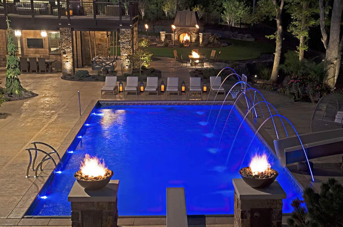 old world lodge style home exterior with a pool at dusk