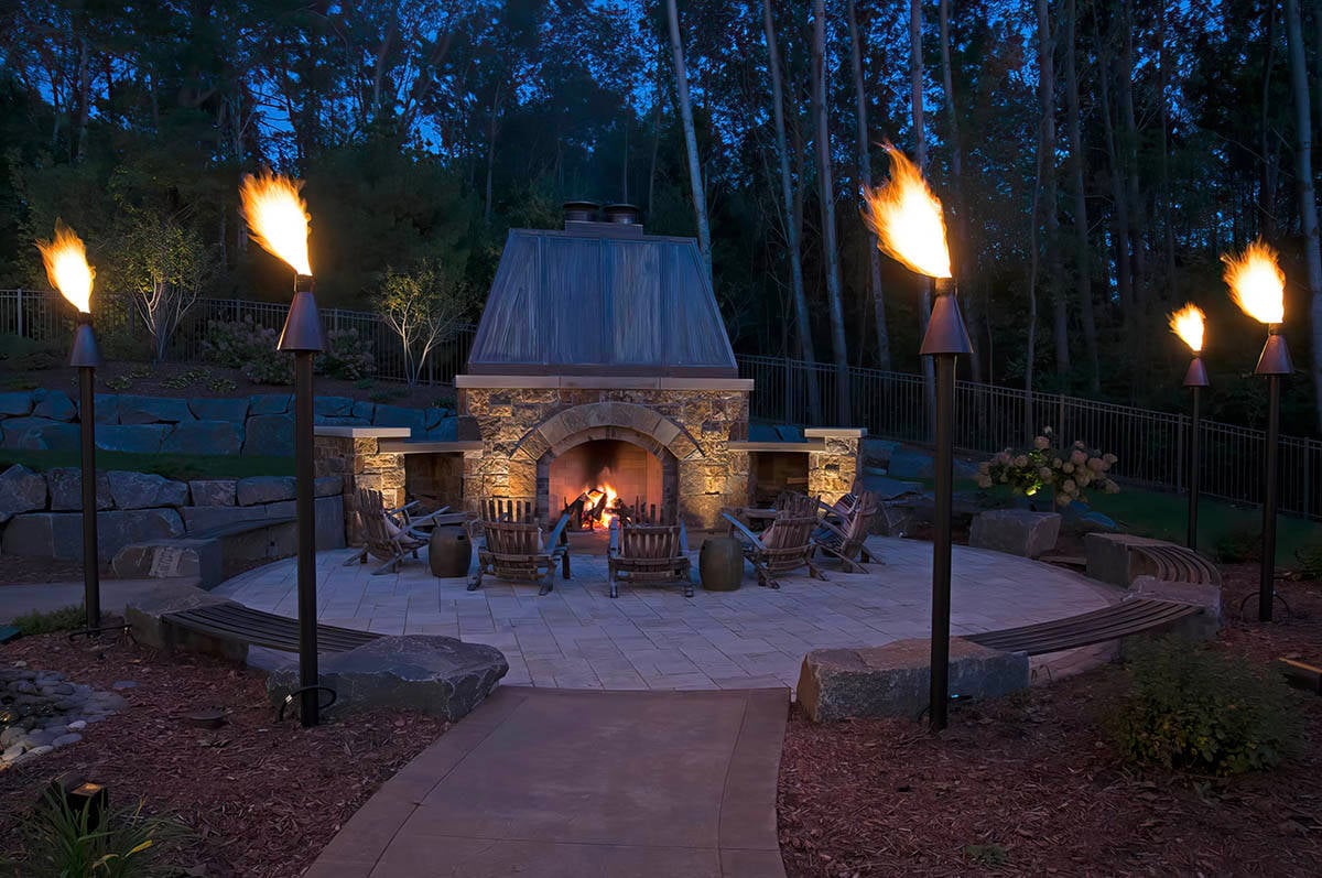 old world lodge style home exterior patio with a backyard fireplace at dusk