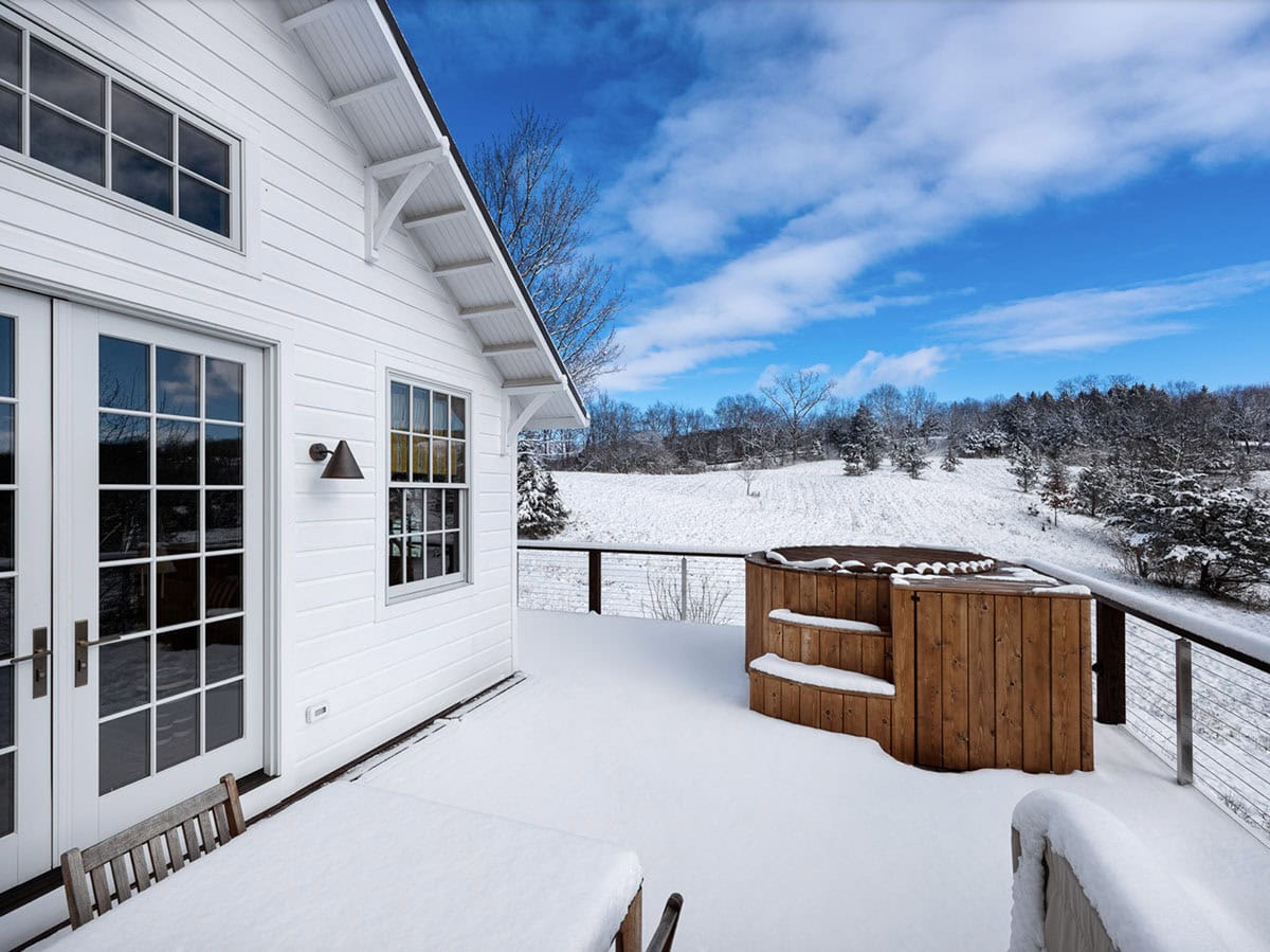 rustic cottage exterior back porch with a hot tub and snow