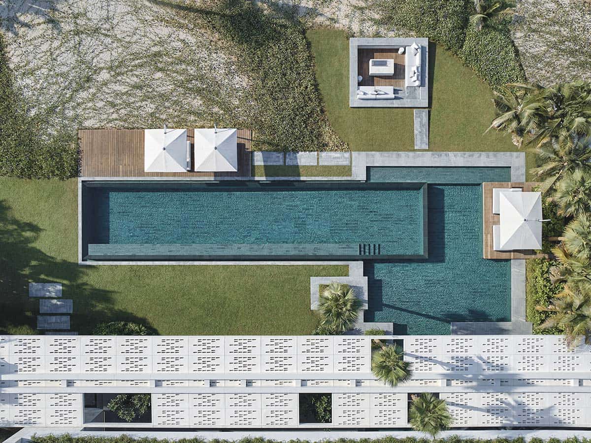 Aerial view of a vibrant pool area adjacent to a sandy beach, surrounded by palm trees and sun loungers