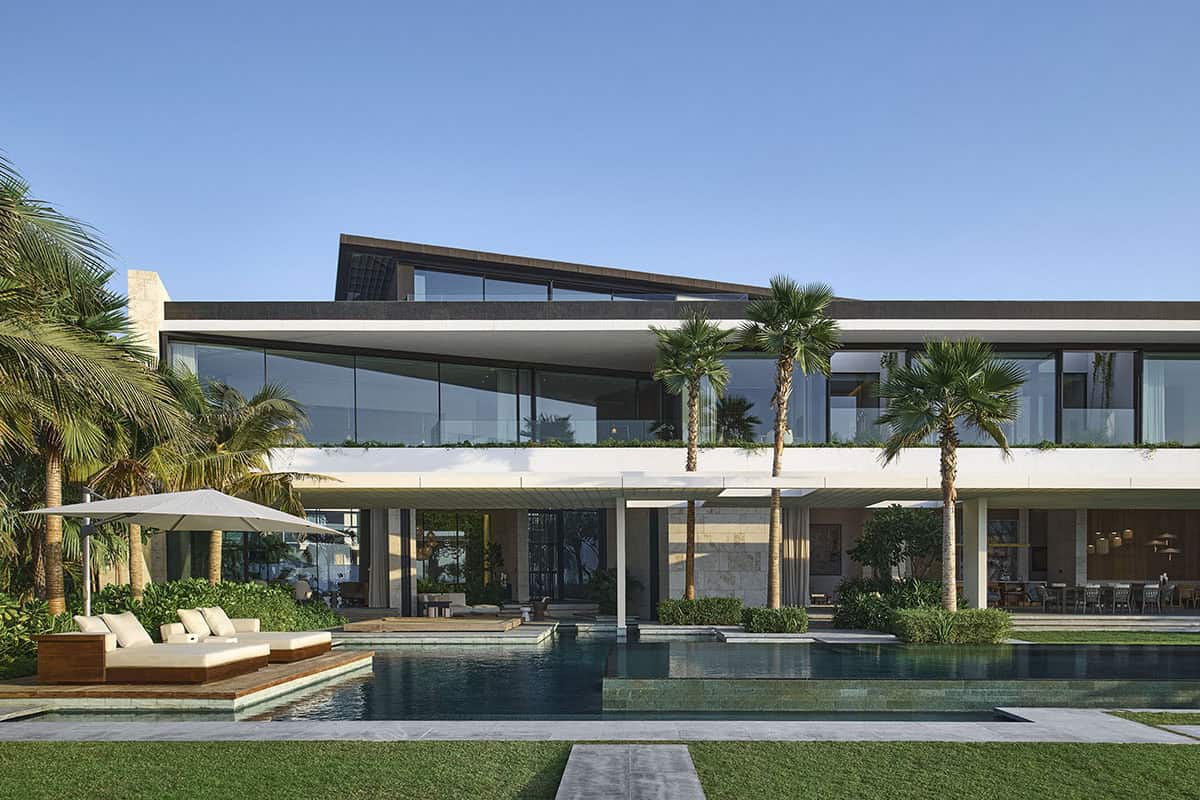 A contemporary home featuring a swimming pool surrounded by palm trees in a sunny outdoor setting