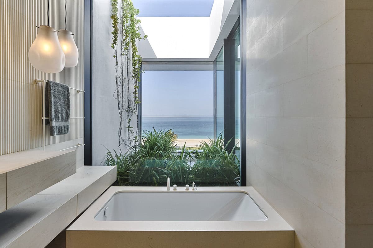 A serene bathroom featuring a large window with a stunning view of the ocean and blue sky