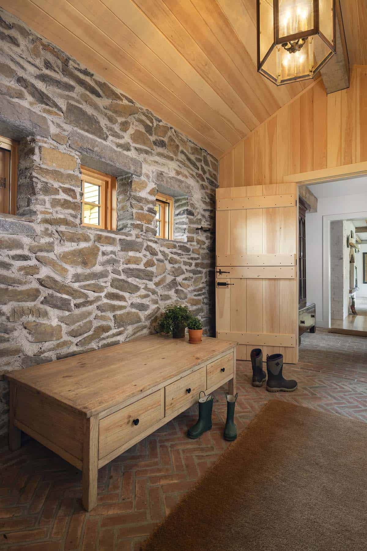 rustic mudroom with a bench seat, stone wall, and herringbone brick flooring