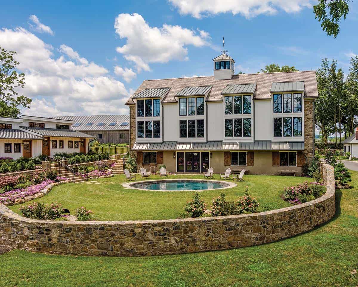 converted stone barn home with pool and curved stone retaining wall, connected white guest wing, weathered gray equipment barn, and rolling Pennsylvania countryside