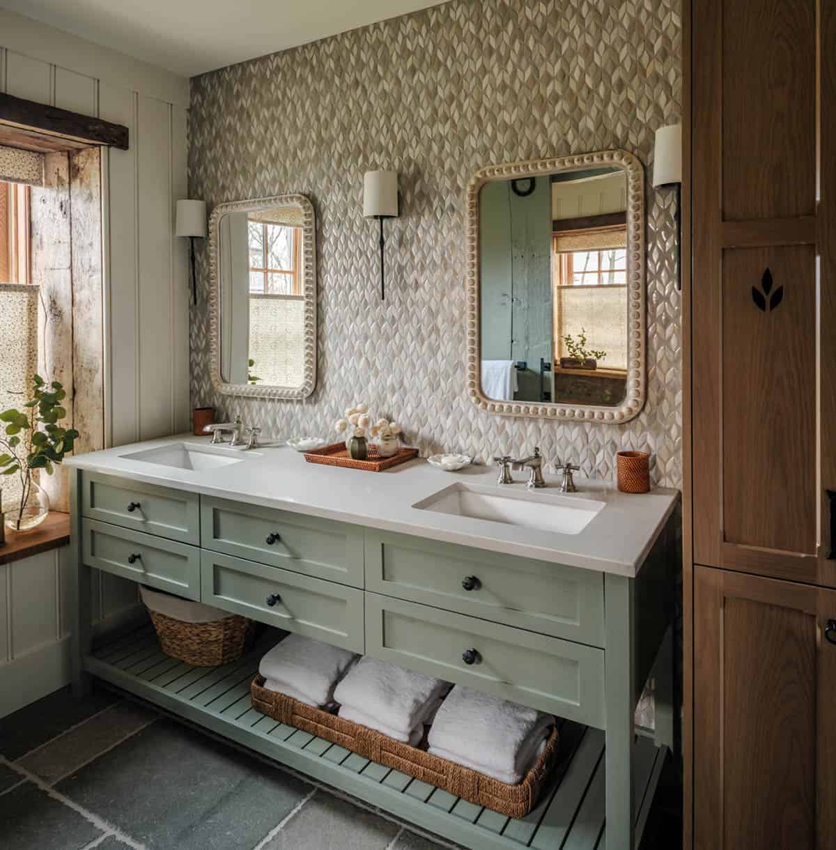 Primary bathroom double vanity with sage green open-shelf cabinet, white quartz countertop, dual undermount sinks with polished nickel fixtures, diamond-pattern textured tile accent wall, beaded frame mirrors, white sconces, and slate tile floor