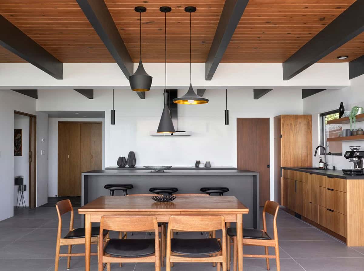 midcentury modern open plan kitchen dining room with black beams teak cabinets and sliding glass doors to Bay view deck
