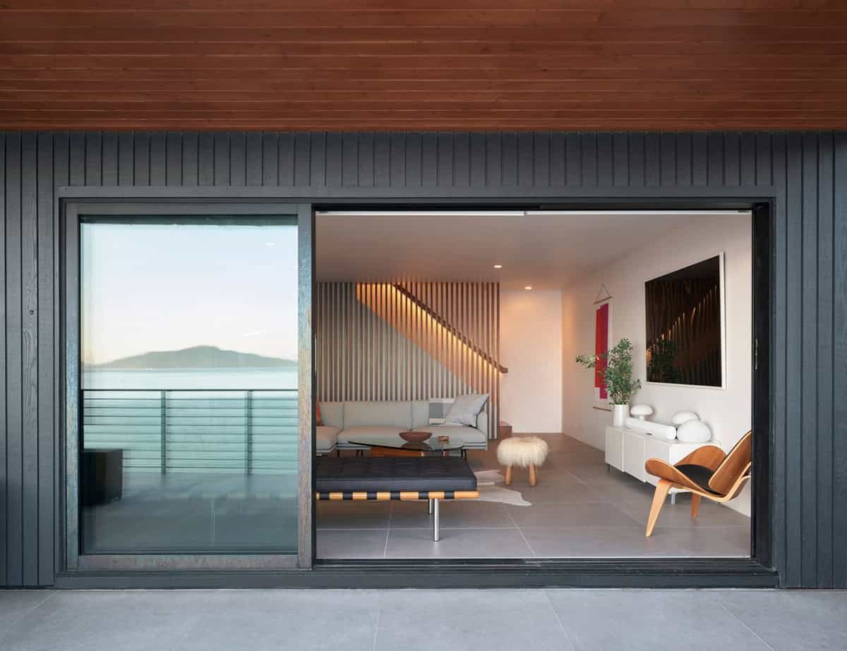 midcentury modern family home exterior at dusk with dark siding sliding glass doors walnut slat stair wall and San Francisco Bay view