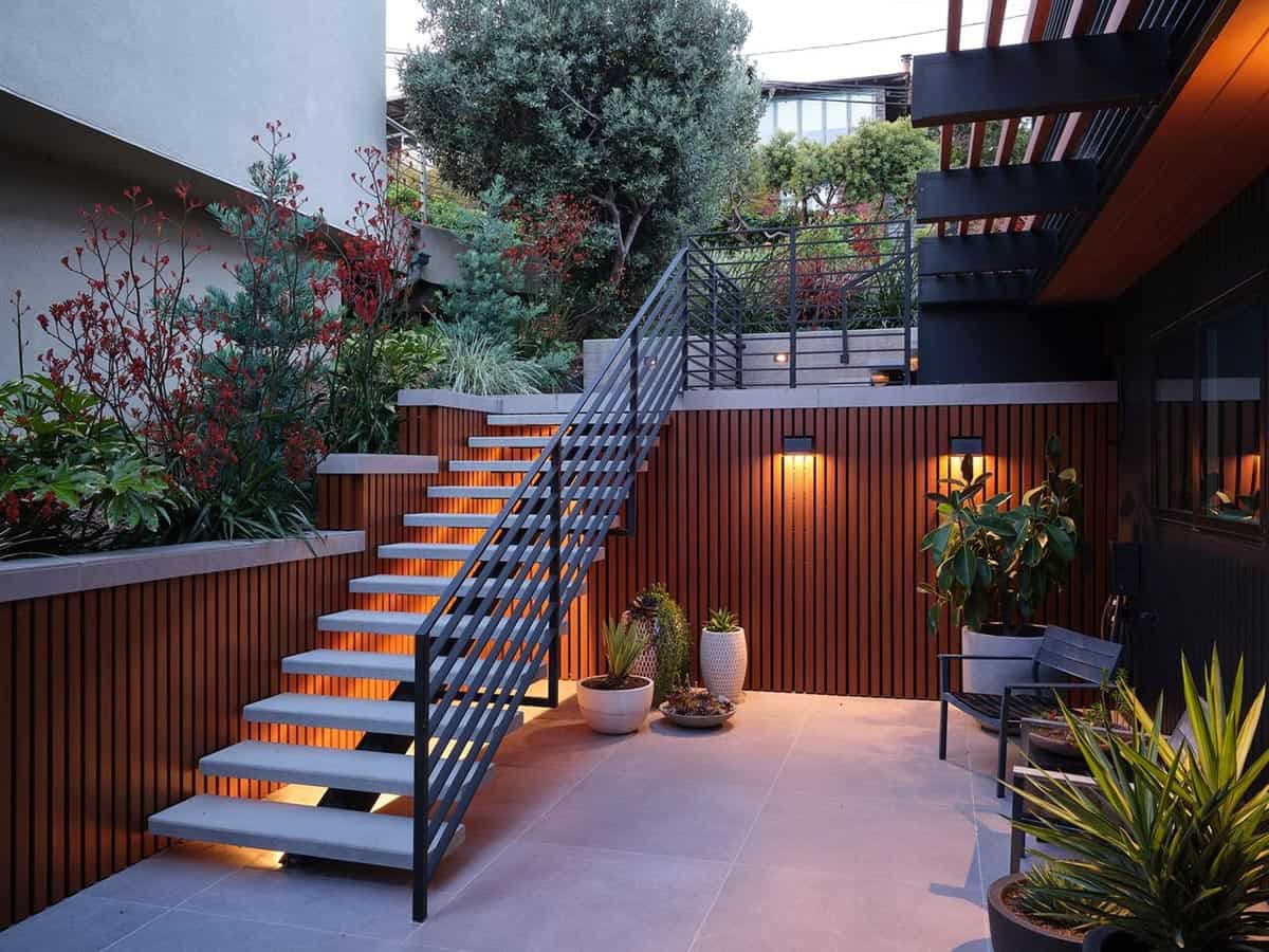 midcentury modern hillside home outdoor patio at dusk with floating concrete stairs black steel railing cedar slat wall and uplighting